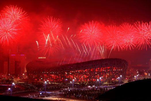 Publiek in de arena tijdens de sluitingsceremonie olympische spelen 2026 met lichtshow en olympische vlaggen
