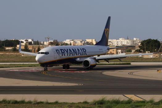 Passagiers bekijken vluchtprijzen van ryanair op laptop terwijl een vertrekbord op de luchthaven op de achtergrond zichtbaar is
